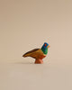 A colorful Handmade Holzwald Pheasant sculpture against a plain beige background, featuring vibrant blue, green, and orange hues with detailed carvings. This piece is an excellent example of sustainable toys.