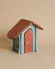 A small wooden Ostheimer Hen House / Chicken Coop with a teal base and roof, perfect for imaginative play. The house has a curved design with a rustic, red-colored door and roof. The wooden texture is visible, giving it the charm of handcrafted wooden toys. The background is a plain beige.