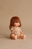 The Minikane Baby Doll (13") - Capucine with Clothing and Stroller Set features a doll with chin-length reddish-brown hair and bangs, wearing a light brown buttoned outfit, seated on a plain beige surface.