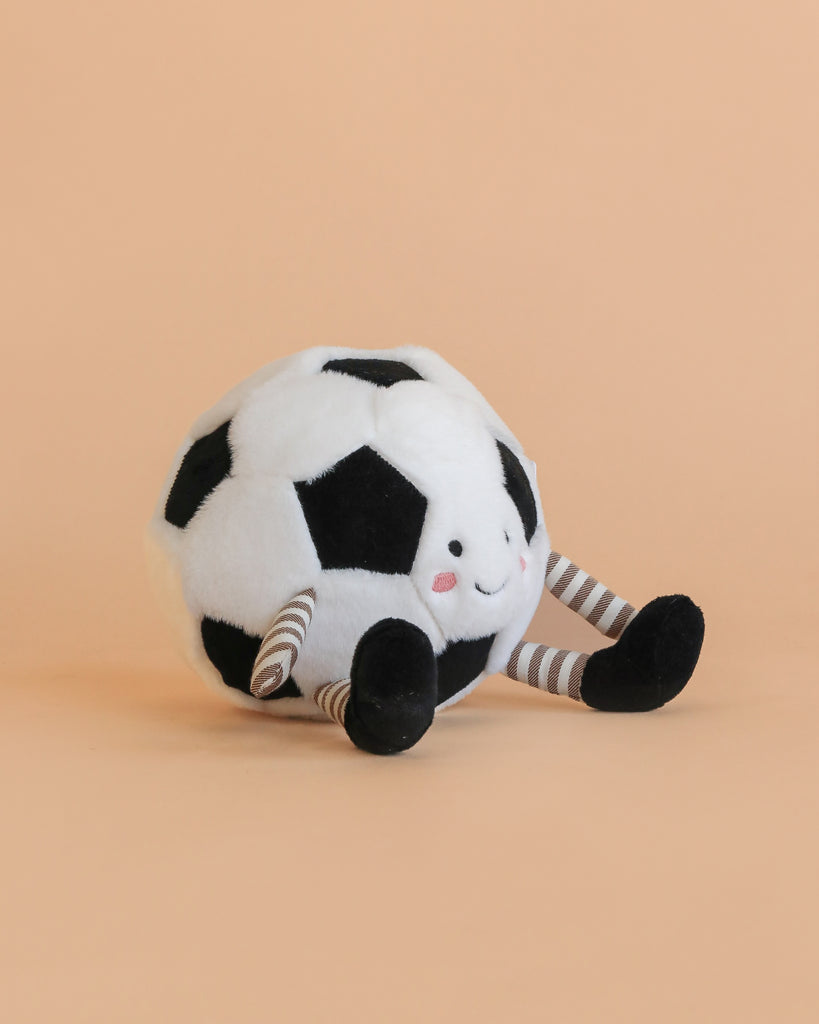 A Mon Ami Soccer Ball Set plush toy featuring a smiling face, rosy cheeks, and striped arms and legs, displayed on a light peach background.
