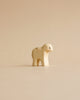 A minimalist cream Holzwald figure from the Handmade Holzwald Shepherd with Farm Animals Set stands on a light beige surface, featuring rounded shapes and a subtle black eye—ideal for fans of sustainable toys.