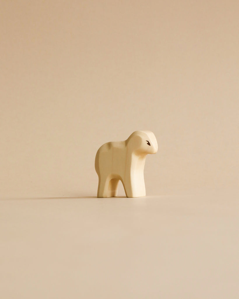 A minimalist cream Holzwald figure from the Handmade Holzwald Shepherd with Farm Animals Set stands on a light beige surface, featuring rounded shapes and a subtle black eye—ideal for fans of sustainable toys.