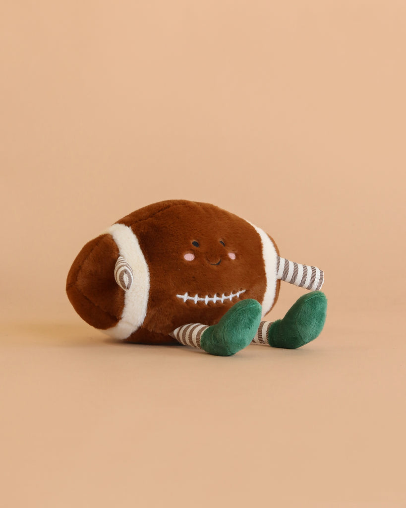 The Mon Ami - Freddie Football Plush Toy, featuring a smiling face, striped arms, and green feet, sits on a plain beige background—making it an adorable cuddle companion or a delightful gift for kids.