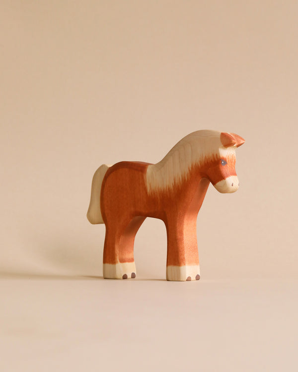A Handmade Holzwald Light Brown Horse with a smooth finish, standing on a plain beige background. Its main color is a warm chestnut with white accents on the mane, tail, and hooves. This sustainable toy