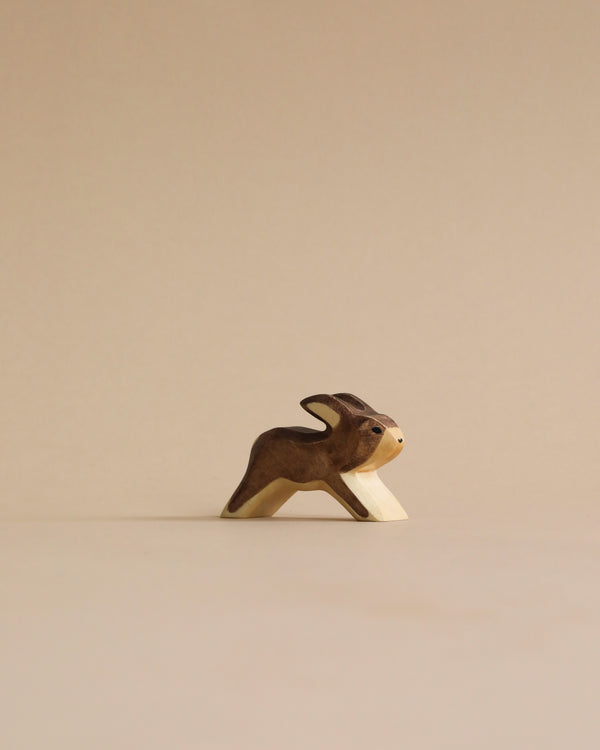 A handmade Holzwald Running Rabbit, crafted with a dark brown body and a light beige face, stands against a plain beige background. This piece is one of the sustainable toys from the Holzwald.