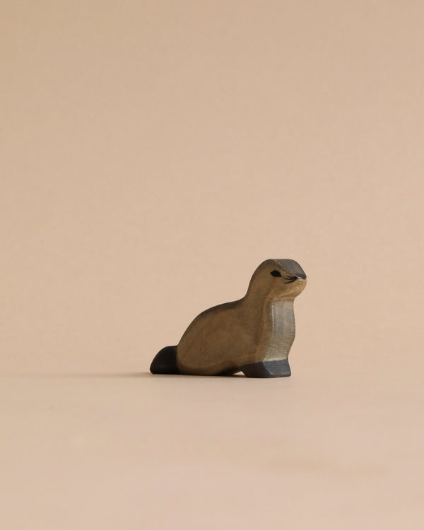 A Handmade Holzwald Baby Sea Lion, crafted from high-quality wood, placed on a plain beige background and captured under soft lighting. The sea lion is carved in a simplistic style with smooth, rounded edges.