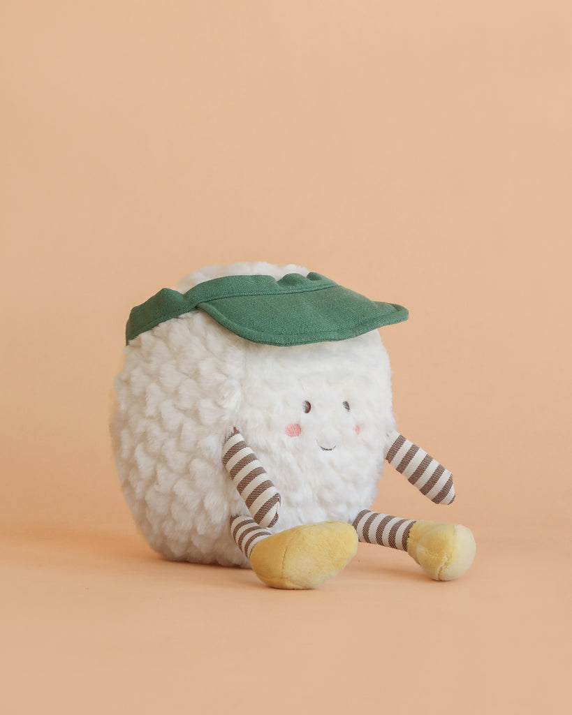 The Mon Ami - TeeTee Golf Ball Plush Toy features a white, textured ball with a green leaf hat, striped arms and legs, yellow feet, and a smiling face with rosy cheeks, shown against a peach background.