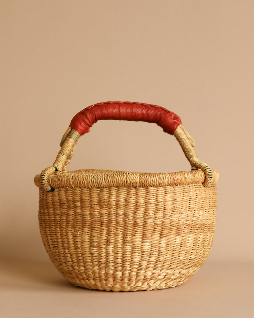 The Easter Basket Gift Set features a round, woven elephant grass basket with a sturdy handle wrapped in red material, displayed against a plain beige background.