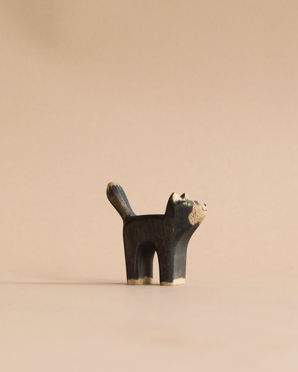 A small, Handmade Holzwald Black Cat figurine, painted in dark colors, standing upright on an educational plain beige background.