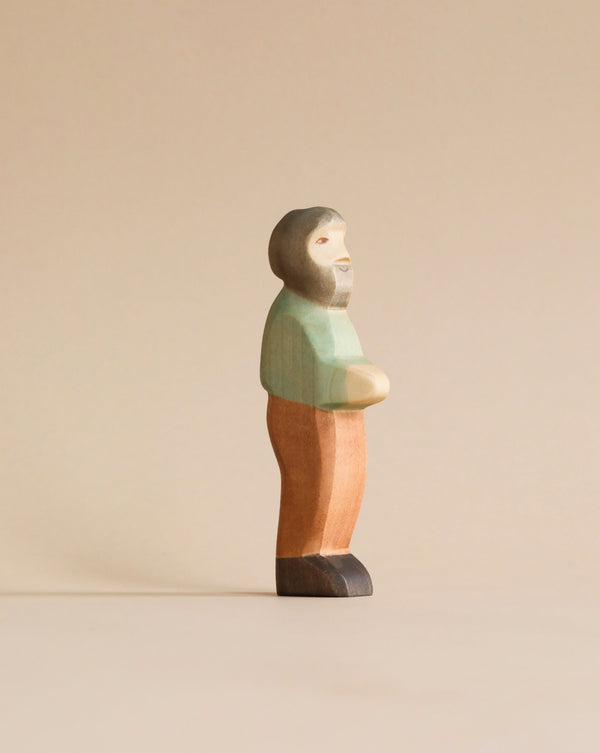 A Handmade Holzwald Grandfather figurine, painted in pastel colors of green, orange, and peach, standing against a plain, light beige background.