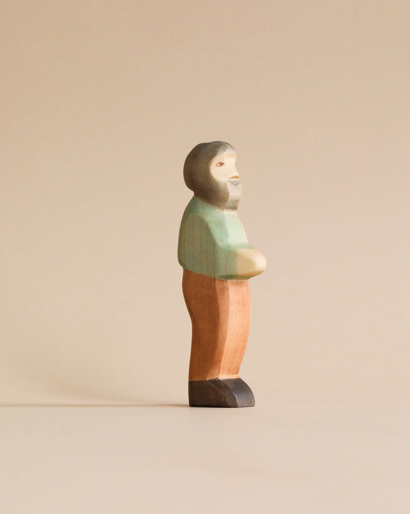 A Handmade Holzwald Grandfather figurine, painted in pastel colors of green, orange, and peach, standing against a plain, light beige background.