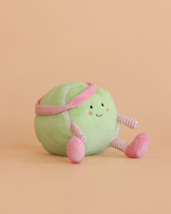 The Mon Ami - Tina Tennis Ball Plush Toy is a cute, round, green plush with a smiling face, pink headband, and pink-striped arms and legs—an ideal gift for tennis fans.