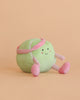 The Mon Ami - Tina Tennis Ball Plush Toy is a cute, round, green plush with a smiling face, pink headband, and pink-striped arms and legs—an ideal gift for tennis fans.