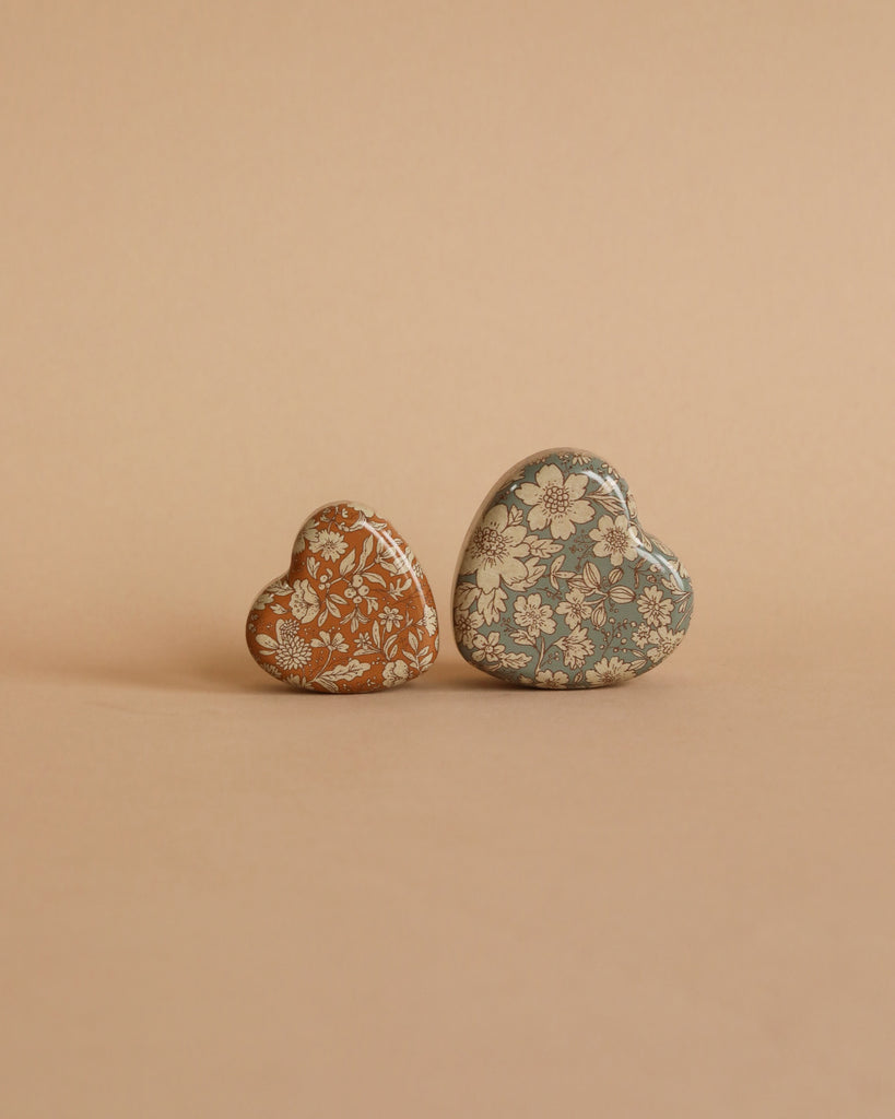 The Maileg LouiMax On the Go Suitcase Set features two heart-shaped cases with floral patterns, one in brown and one in blue, displayed side by side on a light beige background.