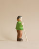 The Handmade Holzwald Shepherd with Farm Animals Set features a wooden shepherd figure in a green shirt and brown pants with a white cane and black cap—ideal for anyone who values sustainable, artisanal toys.