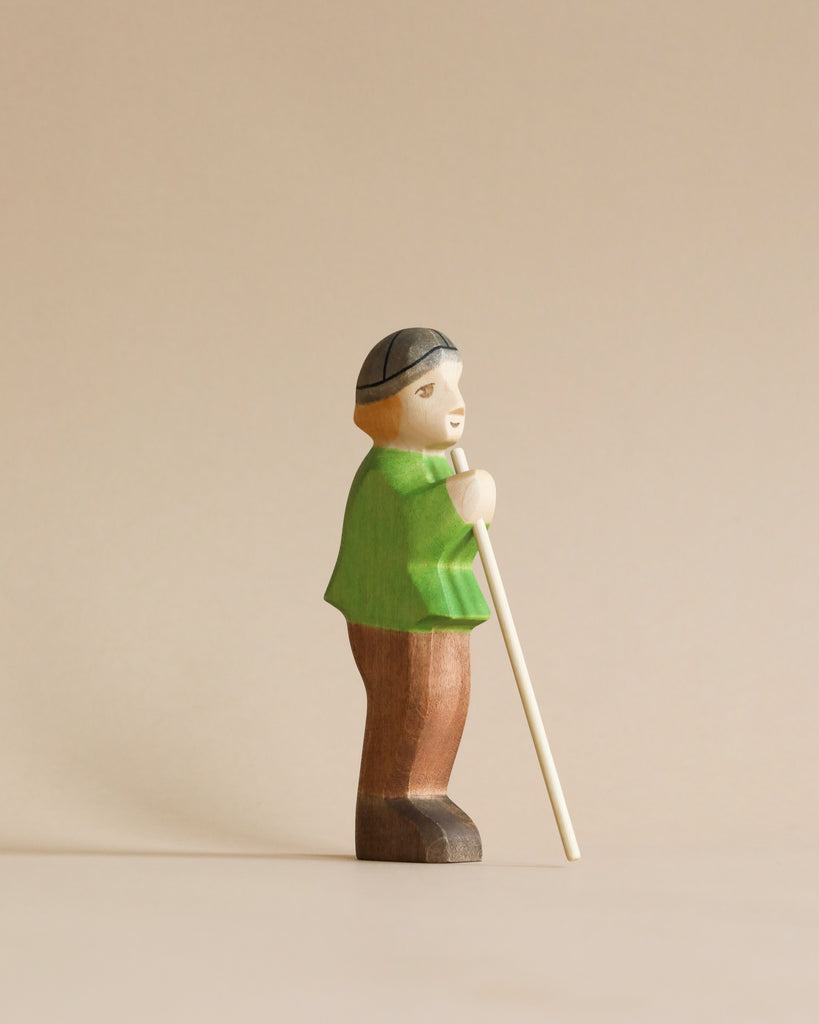 The Handmade Holzwald Shepherd with Farm Animals Set features a wooden shepherd figure in a green shirt and brown pants with a white cane and black cap—ideal for anyone who values sustainable, artisanal toys.
