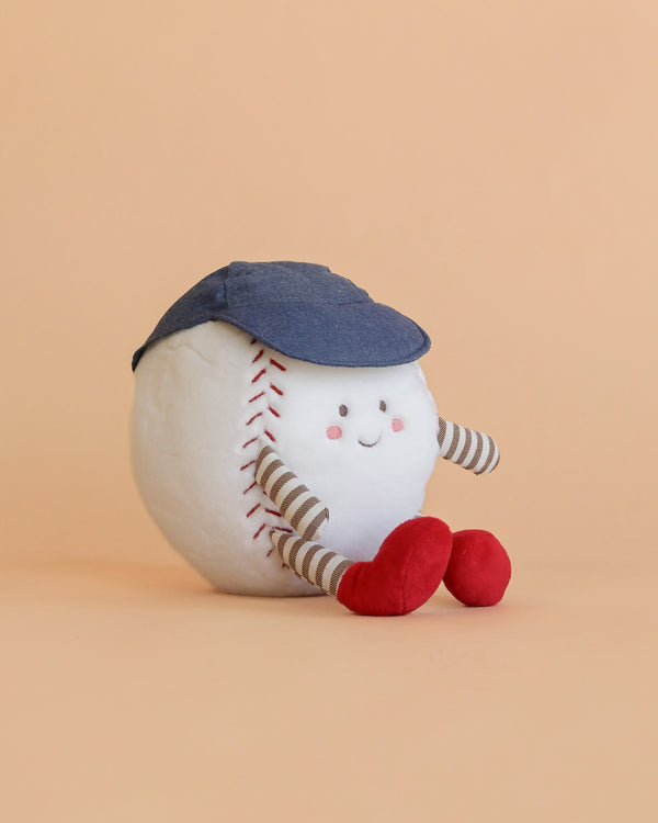The Mon Ami - Buddy Baseball Plush Toy, featuring a smiling face, striped limbs, red feet, and a blue cap, sits on a beige background—a delightful sports-themed gift for any fan.