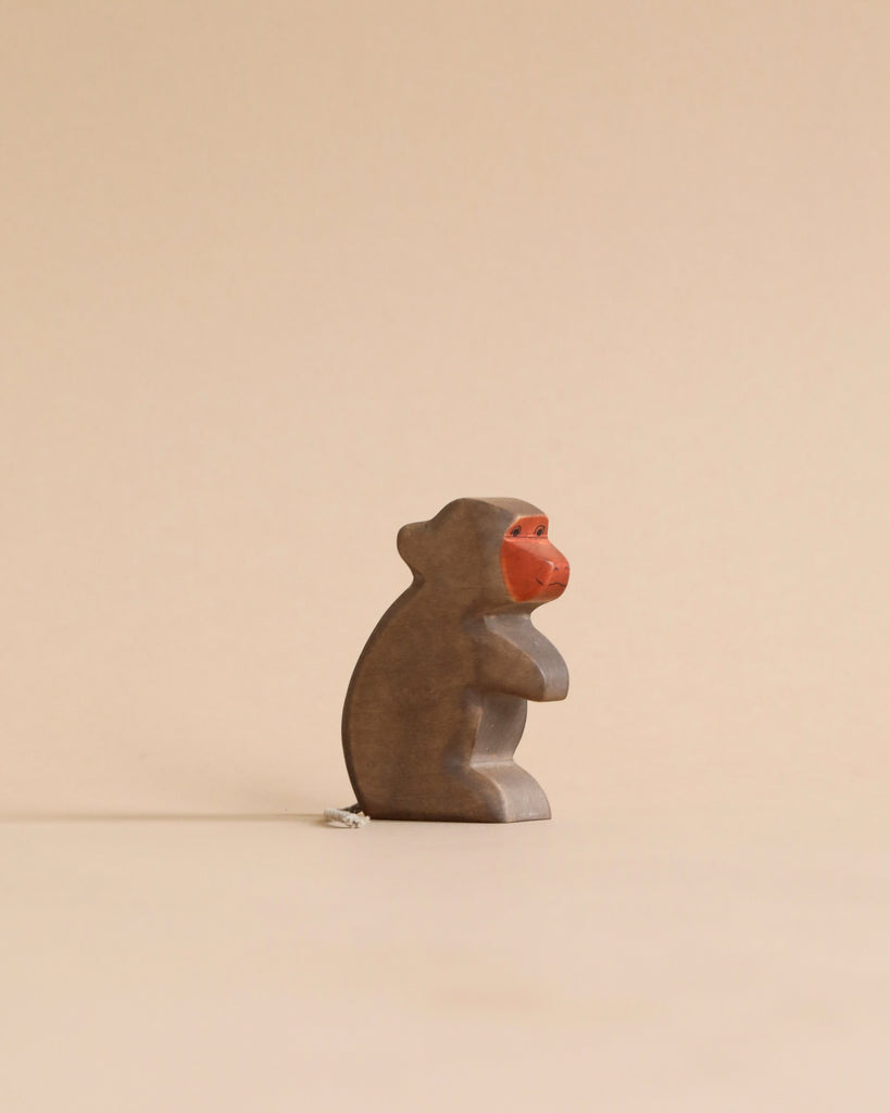 A small, stone monkey statue with a bright red face, sitting in a contemplative pose against a plain, light beige background from Holzwald Brand.
 
Product Name: Handmade Holzwald Baboon
