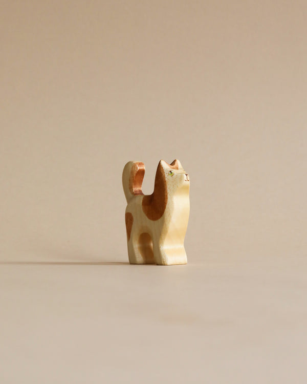 A Handmade Holzwald Cat figurine with a minimalist design, made of high-quality wood, featuring abstract spots and a curved tail, standing against a plain beige background.