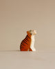 A Handmade Holzwald Sitting Tiger, positioned in a sitting posture with its head turned upward, against a plain beige background. The tiger's body is orange with black stripes.