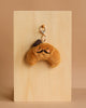 The Mon Ami - Monsieur Croissant Keychain / Bag Charm features a plush croissant with a cute face, rosy cheeks, brown mustache, and small hat—an adorable accessory for your keys or bag. Displayed on a light wooden board with a beige background.