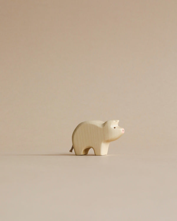 A Handmade Holzwald Piglet figurine stands on a plain beige background, with its small ears perked up and a visible snout and tail, showcasing minimalist art style.