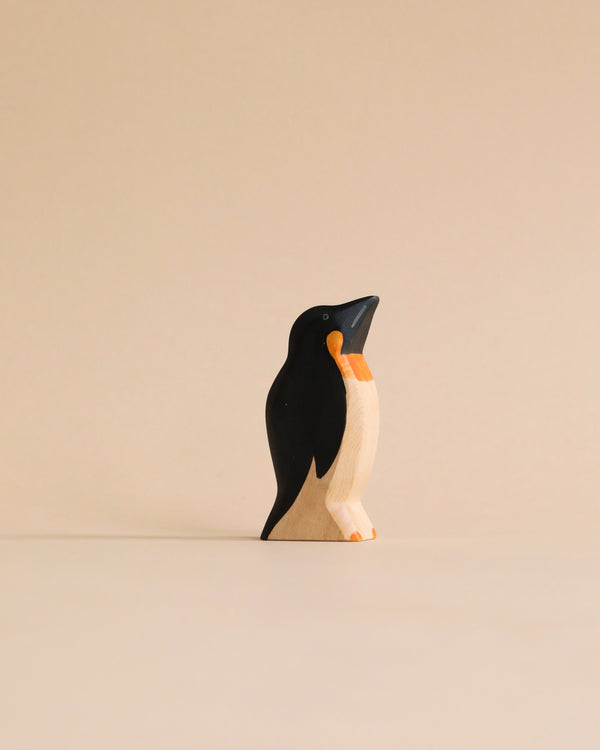 A Handmade Holzwald Penguin figurine depicted standing upright against a plain, light beige background. The figure is stylized, primarily black with white and orange details on the belly and beak. This sustainable toy