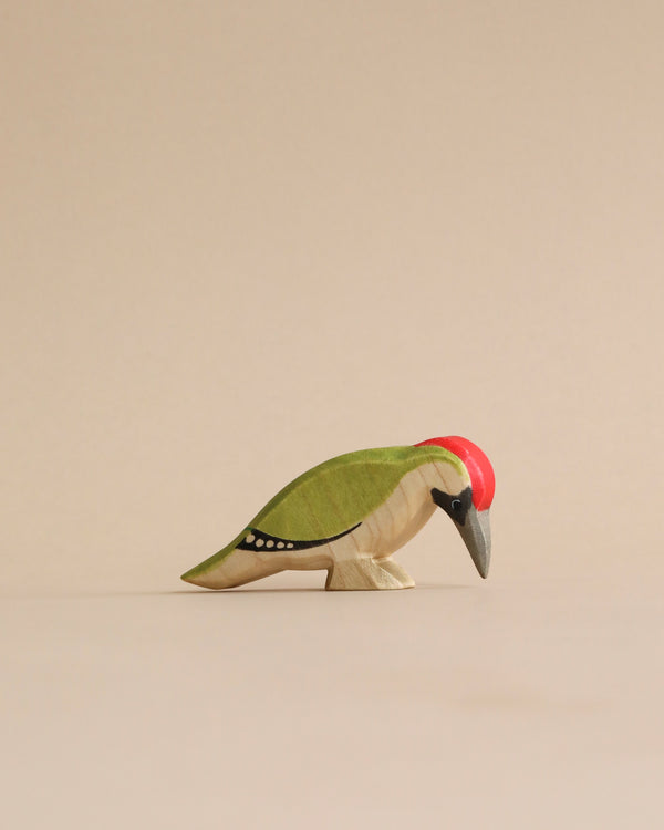 A sustainable Handmade Holzwald Woodpecker Bird figurine with a green body, red head, and detailed wing markings, standing against a plain beige background.
