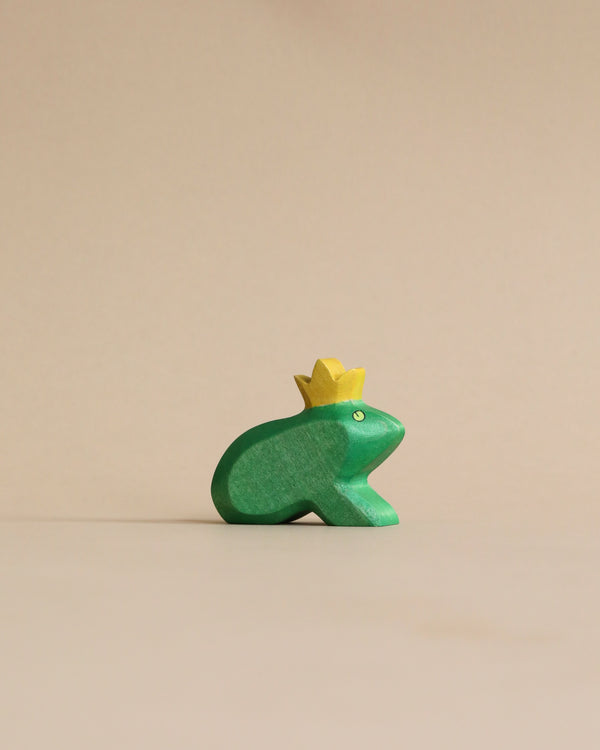 A small, Handmade Holzwald Frog King figurine crafted from sustainable toys, standing against a plain beige background.