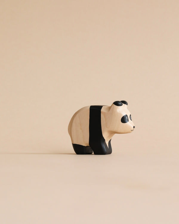 A Handmade Holzwald Baby Panda stands isolated on a beige background, characterized by minimalist design with black and white painted details.