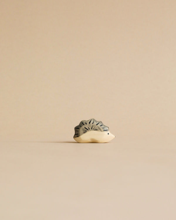 A minimalist image of a small, intricately patterned Handmade Holzwald Hedgehog Baby sculpture with a textured surface, shaped like a star, placed against a light beige background.
