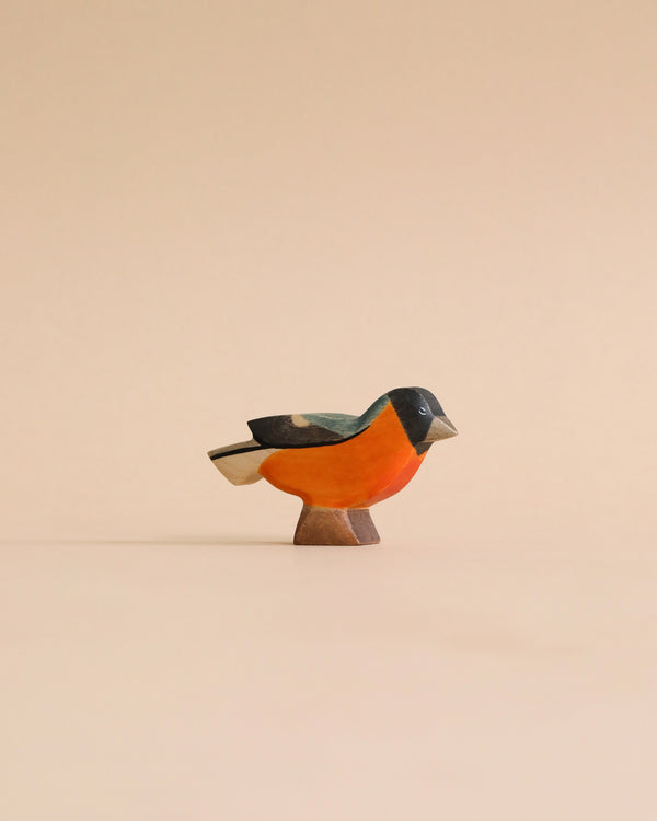 A colorful Handmade Holzwald Bullfinch Bird figurine, with shades of orange and black, stands against a plain beige background. This high-quality figurine is simplistic, featuring smooth curves and minimalistic details.