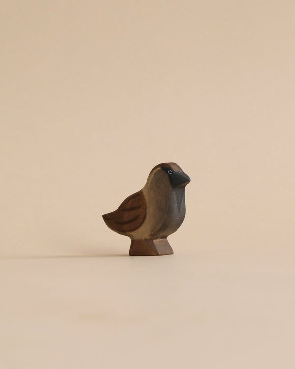 A Handmade Holzwald Sparrow figurine, sculpted in a simplistic style with smooth lines and shaded tones, stands against a plain, light beige background. This piece is an example of sustainable toys, crafted to be