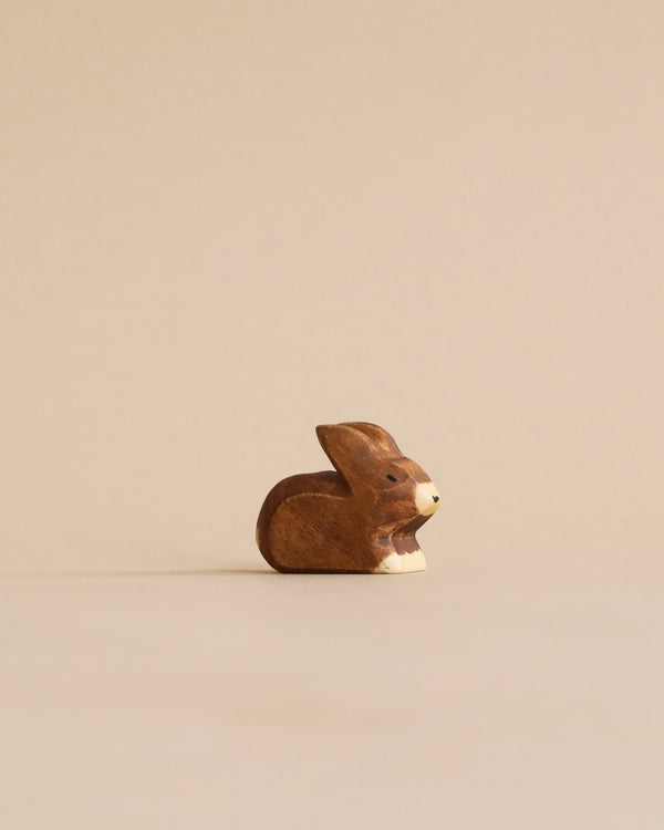 A Handmade Holzwald Small Brown Rabbit figurine placed on a plain, light beige background, giving it a minimalist and serene appearance. This sustainable toy exemplifies eco-friendly craftsmanship.