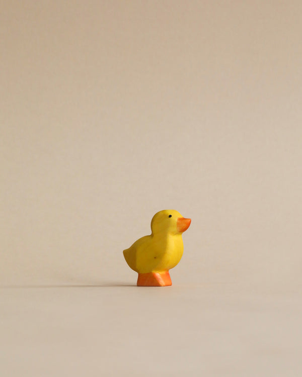 A small yellow Handmade Holzwald Duckling stands isolated against a plain, light beige background, captured in a minimalist style.