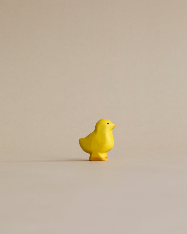 A handmade Holzwald Baby Chick stands alone against a plain, light beige background.