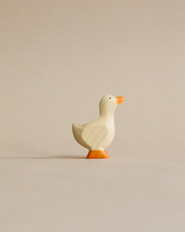 A simple Handmade Holzwald Gosling figurine standing against a neutral beige background. The high-quality duck is painted white with orange feet and a hint of orange on its beak.