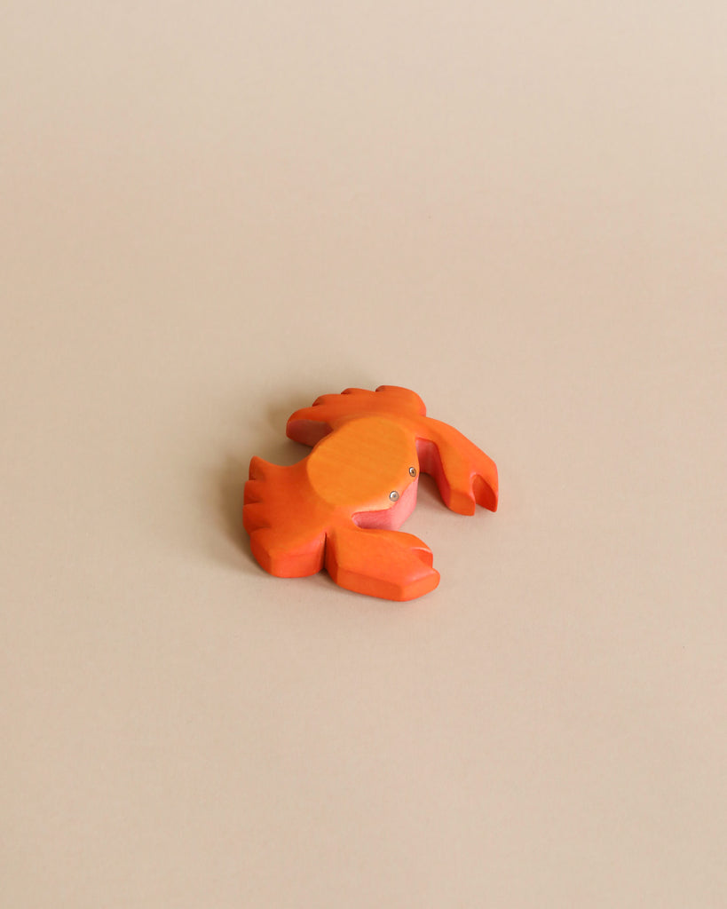 A small, orange crab from the Handmade Holzwald Underwater World Set rests on a beige surface—showcasing handmade wooden sea animals ideal for educational wooden toy collections.