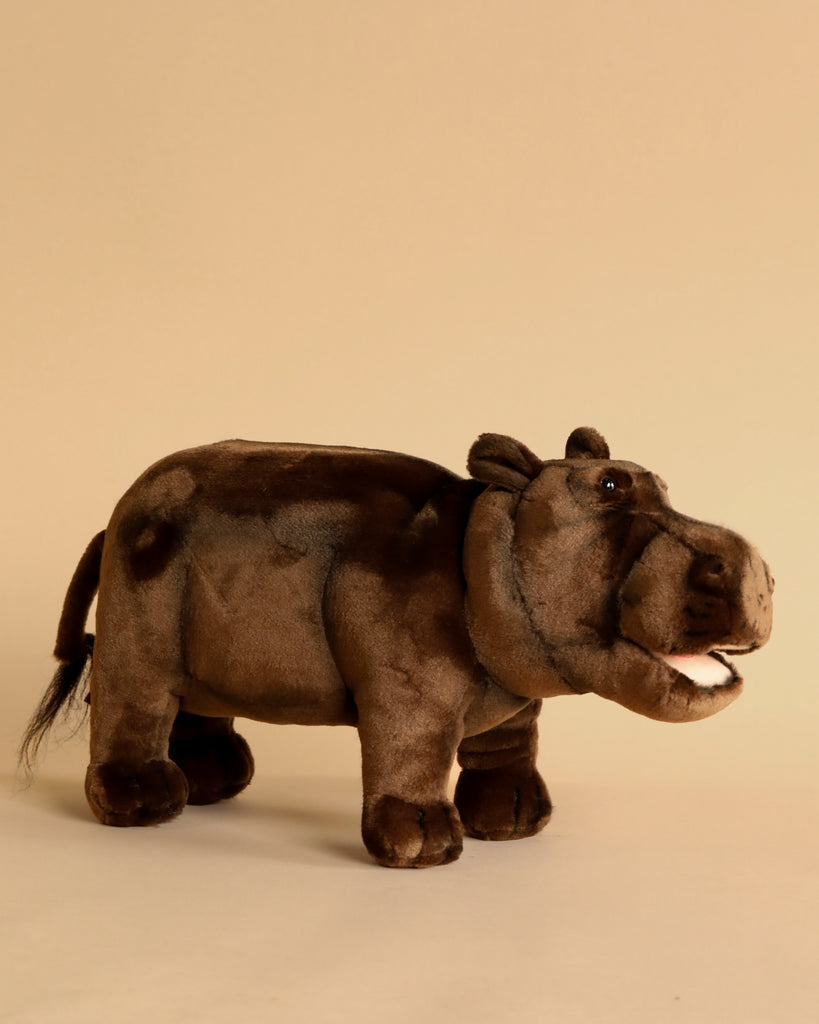 A Happy Hippo Stuffed Animal standing against a plain beige background. The toy is brown with detailed features like eyes, ears, and mouth, capturing a lifelike expression of artisan crafted toys.