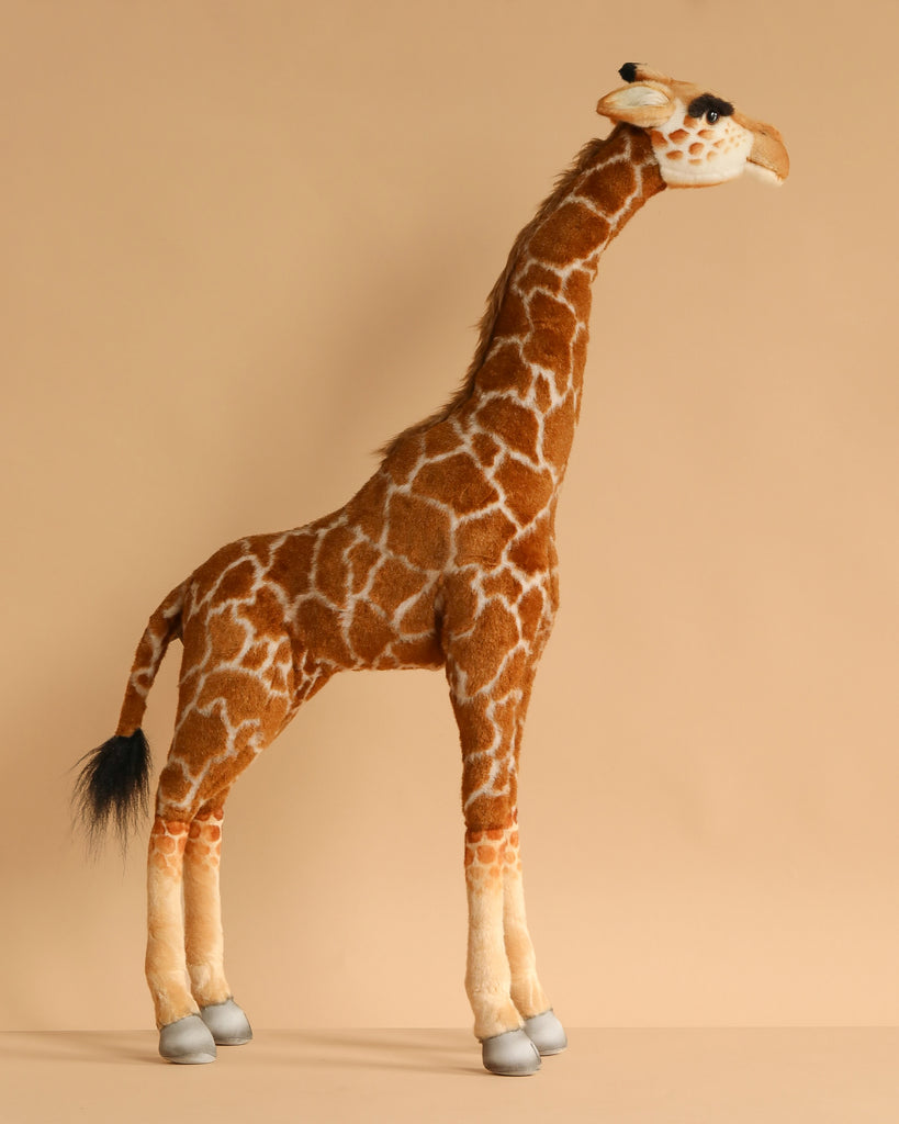 The Medium Giraffe Stuffed Animal, 34''—a hand-sewn plush toy with brown and white fur, a long neck, black tail tip, and gray hooves—stands upright against a beige background. FINAL SALE from HANSA animals.