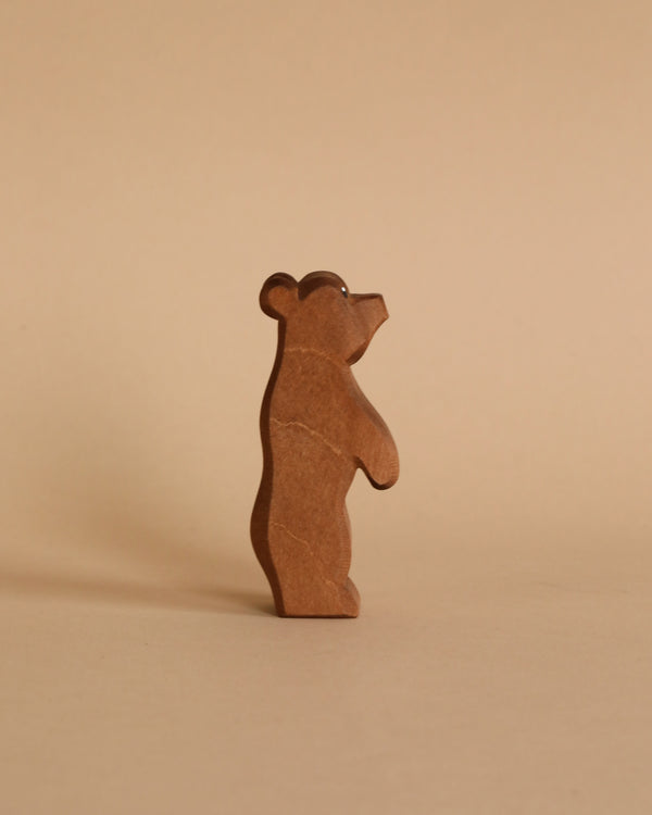 A Ostheimer Small Bear - Standing figure, handcrafted in a minimalist style with visible wood grain texture, stands upright on a plain beige background, appearing to look upward.