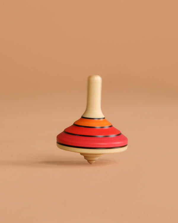 The Mader Small Tango Spinning Top - Red, crafted from maple wood with red, orange, and black stripes, stands upright on a light brown background, highlighting its safe construction and classic design.