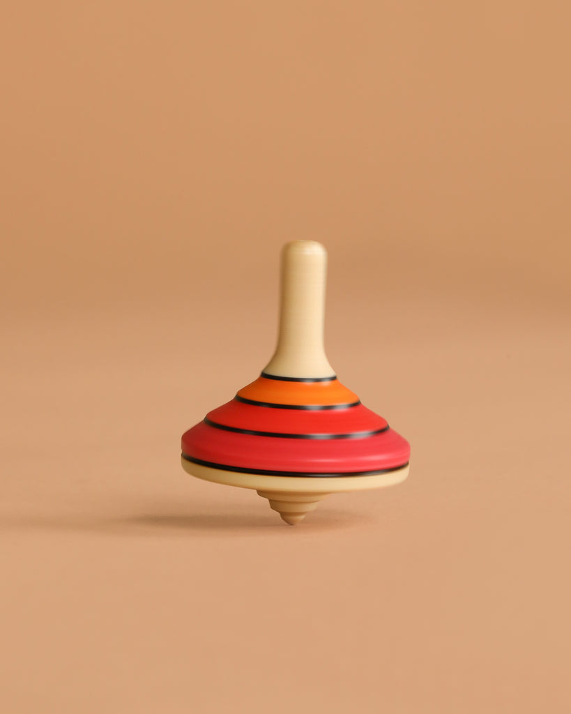 The Mader Small Tango Spinning Top - Red, crafted from maple wood with red, orange, and black stripes, stands upright on a light brown background, highlighting its safe construction and classic design.