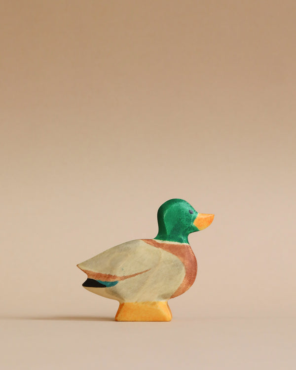 A colorful Handmade Holzwald Male Duck figurine displayed against a plain, light beige background. The duck, crafted from sustainable wood, is painted in shades of green, orange, and beige.