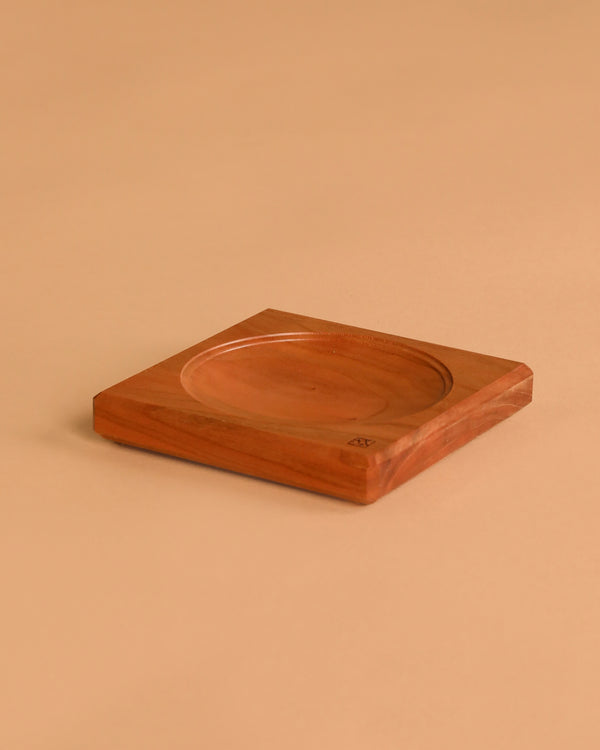 The Mader Cherry Wood Spinning Plate, a square wooden piece with a shallow circular center indentation, rests on a plain beige surface.