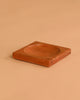 The Mader Cherry Wood Spinning Plate, a square wooden piece with a shallow circular center indentation, rests on a plain beige surface.
