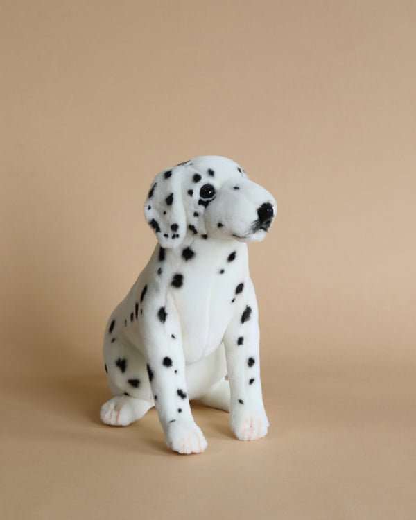 A handcrafted Sitting Dalmatian Dog Stuffed Animal sits against a tan background, featuring distinct black spots over its white body, perked-up ears, and a lifelike pose.