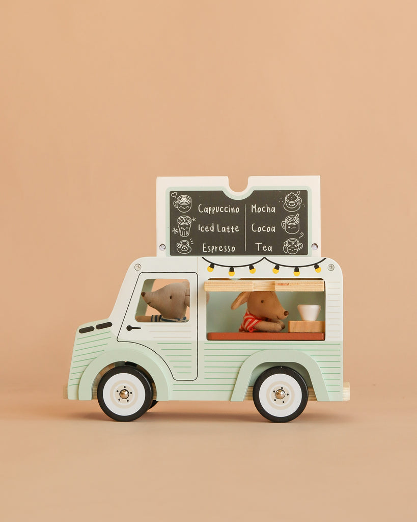 The Maileg Café Van Set includes a pastel green van with Little Brother and Sister Mice figures inside, a chalkboard menu showing cappuccino and mocha, string lights on the window, and a plain beige background.