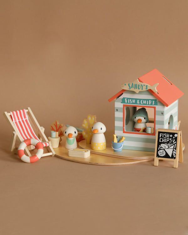 Miniature beach-themed setup with a Sandy's Beach Hut named "Sandy's," crafted from sustainable wood, accompanied by two rubber ducks, a striped deck chair, lifebuoy, potted