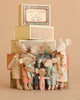 A group from the Maileg Mouse Family Collection, dressed in colorful pajamas and dresses, stand before a stack of Maileg matchbox decorations against a warm, neutral background.